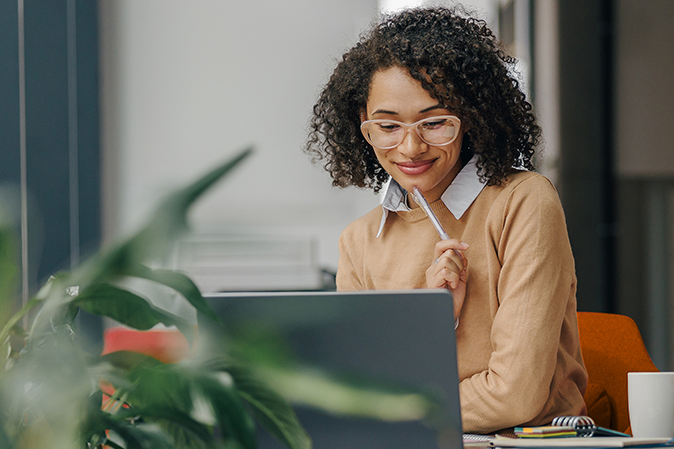 Stylish business woman in eyeglasses working on laptop while sitting in modern office near window